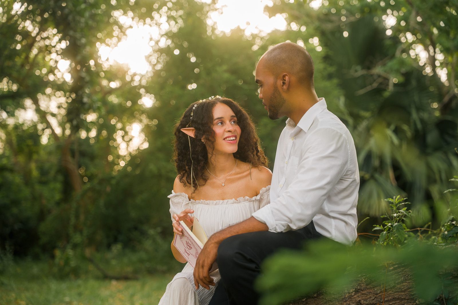 Sidony and Jourdan sitting together in a sunlit garden, looking at one another.