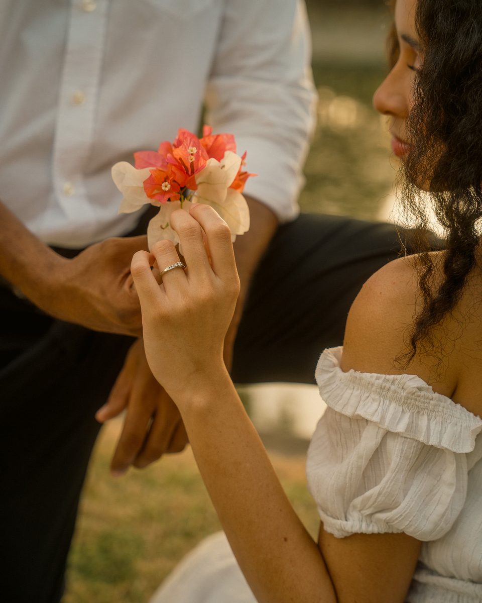 Her hand with the engagement ring, holding a sprig of coral bougainvillea.