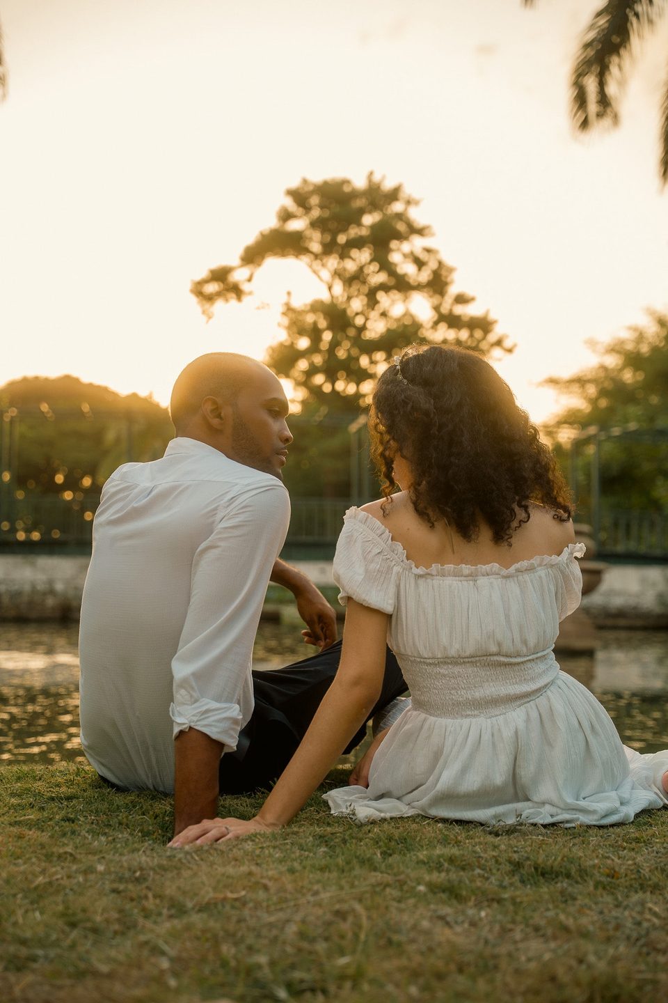 The couple sitting on the grass at sunset, backs to the camera, looking at each other.